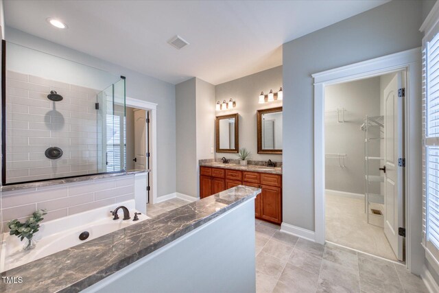 full bathroom with tile patterned flooring, double vanity, a tile shower, a walk in closet, and baseboards