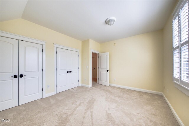 unfurnished bedroom with two closets, light colored carpet, multiple windows, baseboards, and vaulted ceiling