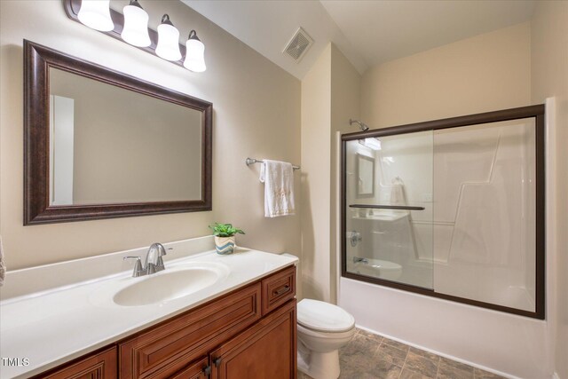 bathroom with toilet, vanity, bath / shower combo with glass door, and stone finish floors