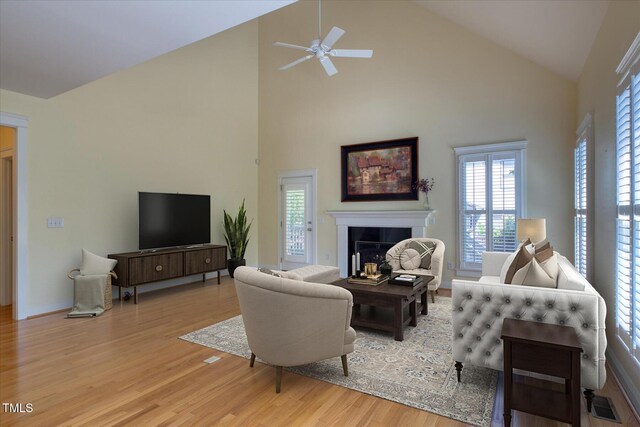 living room with light wood-type flooring, a ceiling fan, high vaulted ceiling, healthy amount of natural light, and a fireplace