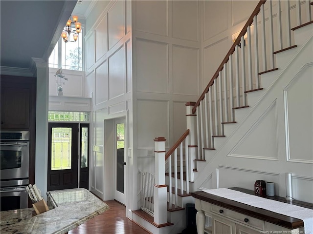 foyer entrance with a notable chandelier, dark wood-style flooring, ornamental molding, stairs, and a decorative wall