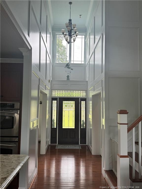 foyer entrance featuring ornamental molding, a chandelier, a decorative wall, and a towering ceiling
