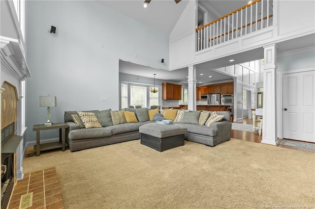carpeted living area featuring a tile fireplace, high vaulted ceiling, and decorative columns