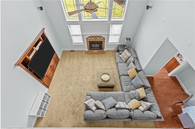 living room featuring visible vents, a ceiling fan, a high ceiling, baseboards, and a tiled fireplace