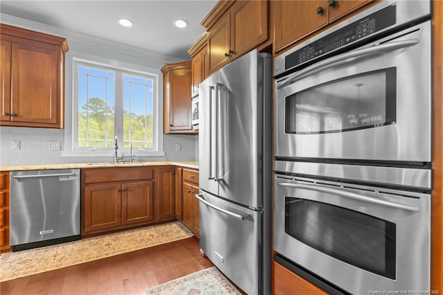 kitchen with a sink, stainless steel appliances, brown cabinets, ornamental molding, and dark wood finished floors