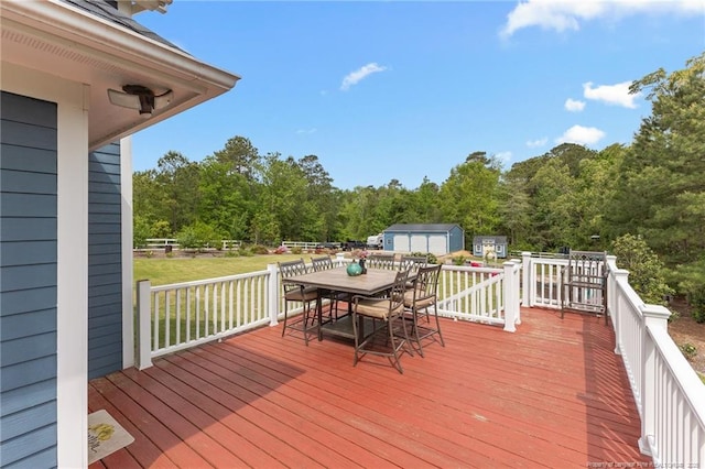 deck featuring a yard, outdoor dining area, a forest view, and an outbuilding