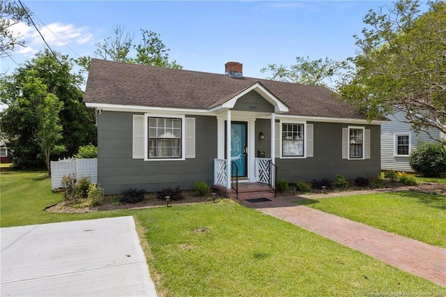 bungalow featuring a chimney, roof with shingles, and a front lawn