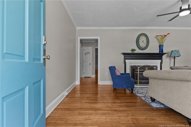 living room featuring a ceiling fan, crown molding, wood finished floors, a fireplace, and baseboards