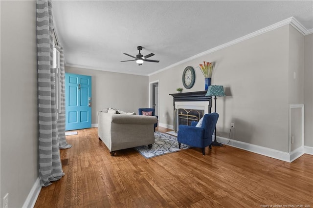 living area featuring a fireplace with flush hearth, wood finished floors, ornamental molding, baseboards, and ceiling fan