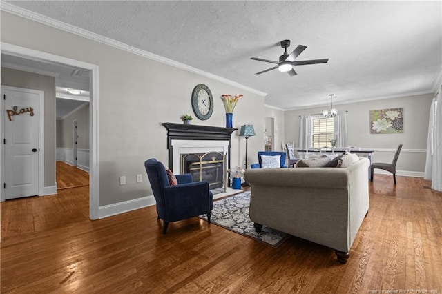 living room featuring a ceiling fan, wood finished floors, crown molding, a fireplace with flush hearth, and baseboards