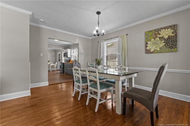 dining space featuring a chandelier, wood finished floors, baseboards, and ornamental molding