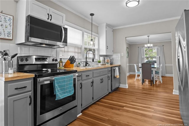 kitchen with appliances with stainless steel finishes, a sink, a chandelier, light wood-style floors, and decorative backsplash