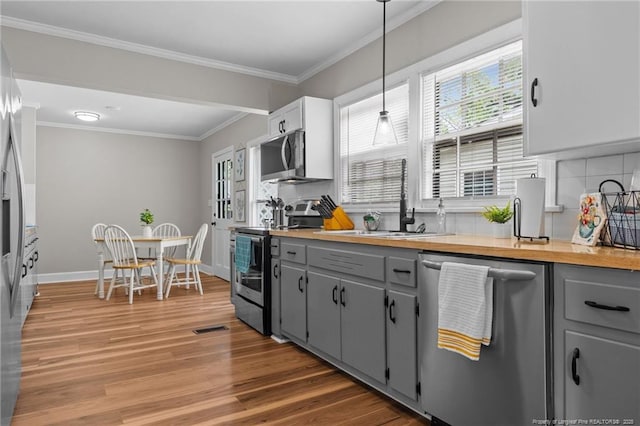 kitchen with appliances with stainless steel finishes, gray cabinetry, a sink, light wood finished floors, and crown molding