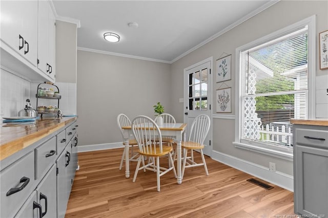 dining room featuring baseboards, ornamental molding, plenty of natural light, and light wood-style floors