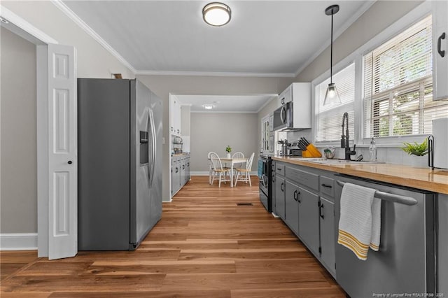 kitchen featuring a sink, ornamental molding, light wood-type flooring, and appliances with stainless steel finishes