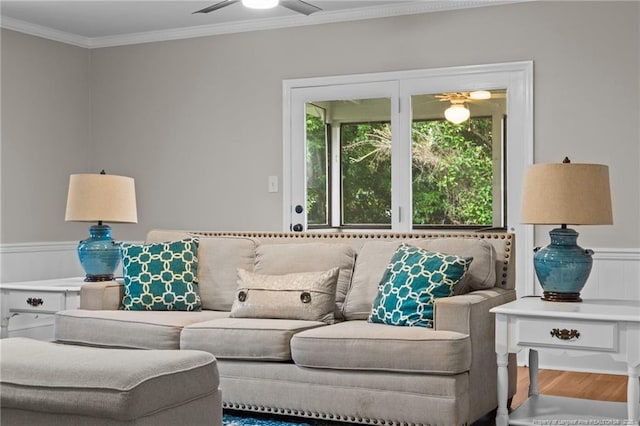 living area with a ceiling fan, wood finished floors, wainscoting, and ornamental molding