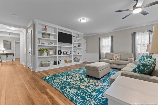 living room with light wood-style floors, wainscoting, a ceiling fan, and ornamental molding