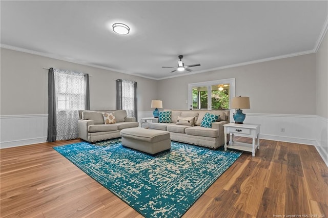 living room with crown molding, wood finished floors, wainscoting, and ceiling fan
