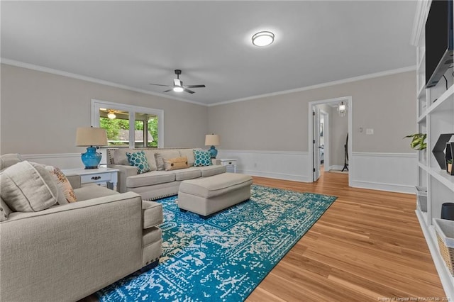 living area featuring light wood-type flooring, ornamental molding, wainscoting, and ceiling fan