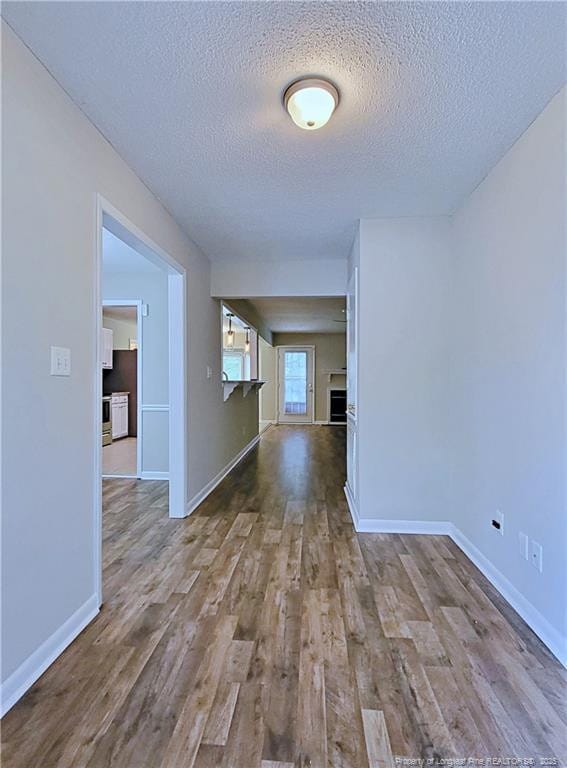 hallway featuring a textured ceiling, baseboards, and wood finished floors