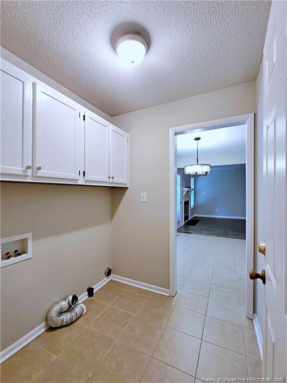 washroom with a textured ceiling, baseboards, an inviting chandelier, light tile patterned flooring, and cabinet space