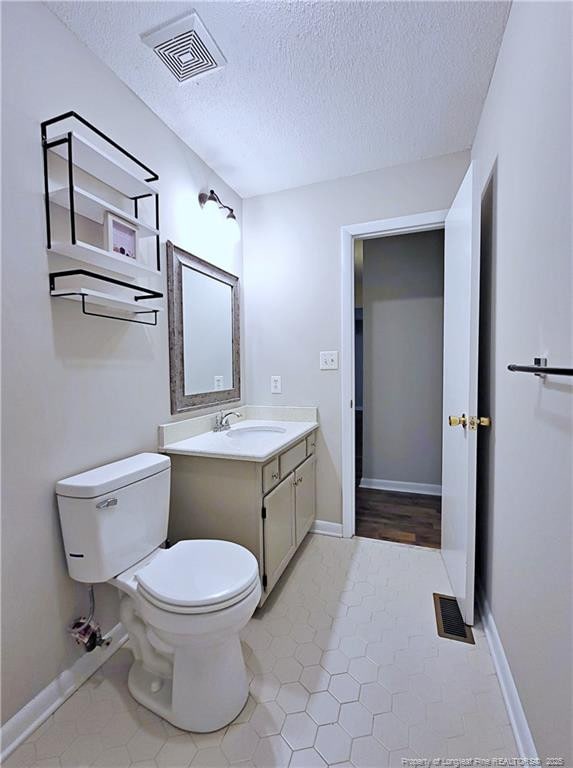 bathroom with toilet, vanity, visible vents, and a textured ceiling