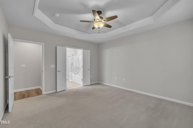 unfurnished bedroom with a raised ceiling, carpet flooring, baseboards, connected bathroom, and a ceiling fan