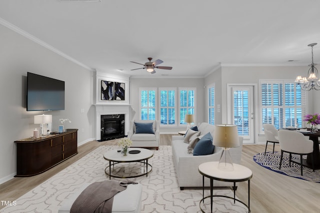 living room featuring light wood finished floors, a fireplace, plenty of natural light, ornamental molding, and a ceiling fan