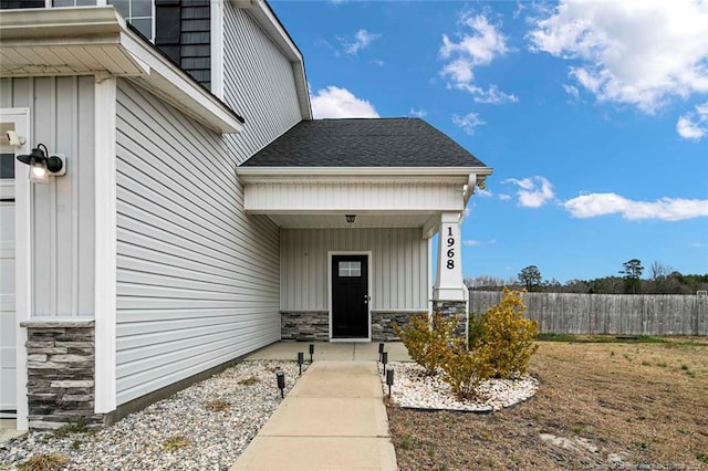 property entrance featuring board and batten siding, stone siding, fence, and roof with shingles