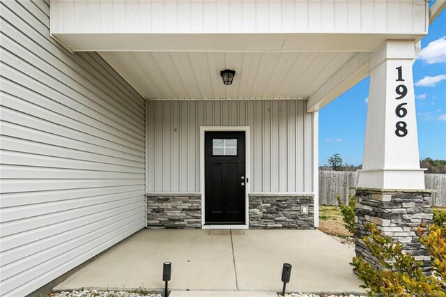 doorway to property featuring stone siding, fence, a patio area, and board and batten siding