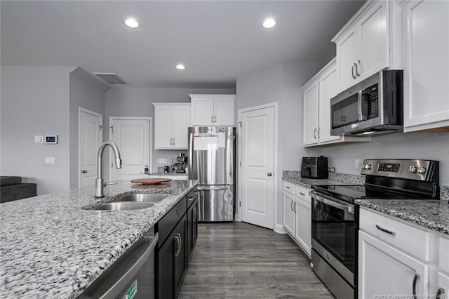 kitchen with appliances with stainless steel finishes, a sink, white cabinets, dark wood-style floors, and light stone counters