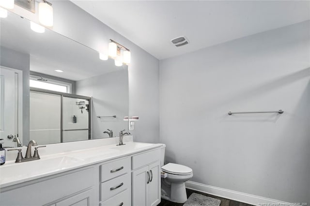 bathroom with a stall shower, toilet, double vanity, baseboards, and wood finished floors