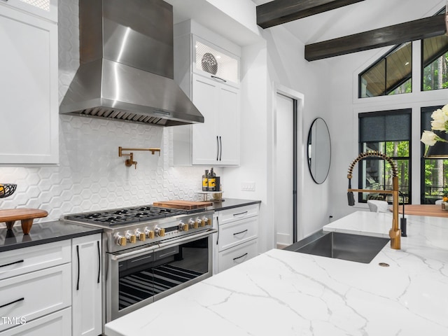 604 Dappled Pine Ave, Durham, NC 27713 - kitchen with wall chimney exhaust hood, range with two ovens, a sink, white cabinets, and beamed ceiling
