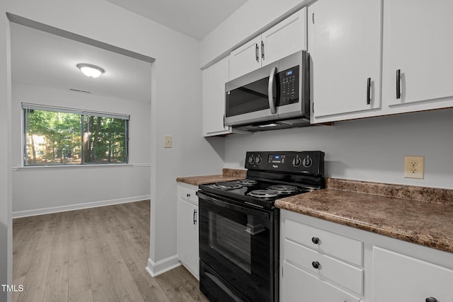 1131 Schaub Dr, Raleigh, NC 27606 - kitchen featuring stainless steel microwave, black electric range oven, light wood-type flooring, white cabinets, and dark countertops