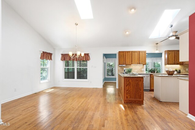 kitchen with a skylight, stainless steel dishwasher, brown cabinetry, tasteful backsplash, and vaulted ceiling