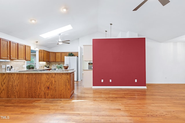kitchen with ceiling fan, white refrigerator with ice dispenser, brown cabinetry, pendant lighting, and a skylight