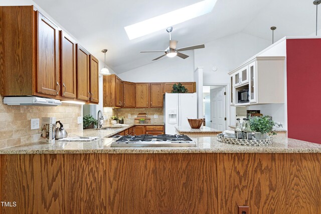kitchen featuring a sink, stainless steel gas stovetop, brown cabinetry, white fridge with ice dispenser, and a skylight