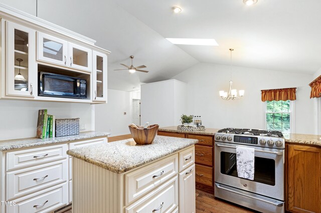 kitchen with gas stove, black microwave, vaulted ceiling, a kitchen island, and glass insert cabinets
