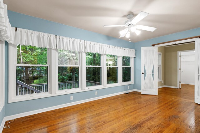 unfurnished room with wood finished floors, baseboards, a ceiling fan, and healthy amount of natural light