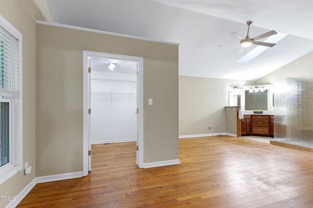 unfurnished bedroom with a skylight, light wood finished floors, lofted ceiling, baseboards, and a spacious closet