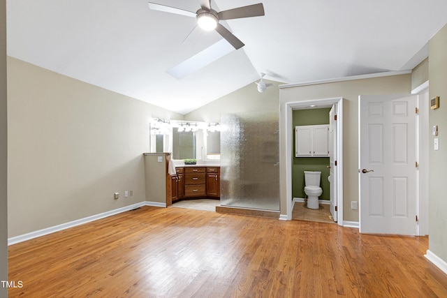 unfurnished bedroom featuring vaulted ceiling, light wood-type flooring, baseboards, connected bathroom, and a skylight
