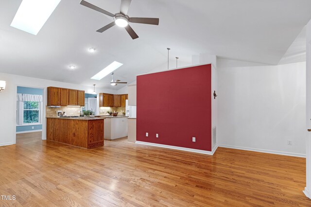 kitchen with a skylight, brown cabinets, a ceiling fan, open floor plan, and baseboards