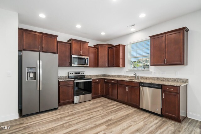 kitchen featuring appliances with stainless steel finishes, a sink, light wood-style floors, light stone countertops, and baseboards