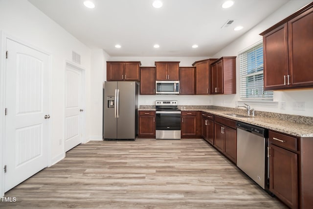 kitchen featuring appliances with stainless steel finishes, recessed lighting, a sink, light stone counters, and light wood-style flooring