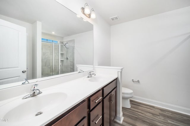 bathroom with toilet, a tile shower, wood finished floors, baseboards, and double vanity