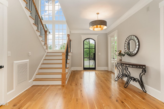 entrance foyer with stairs, light wood finished floors, crown molding, and baseboards