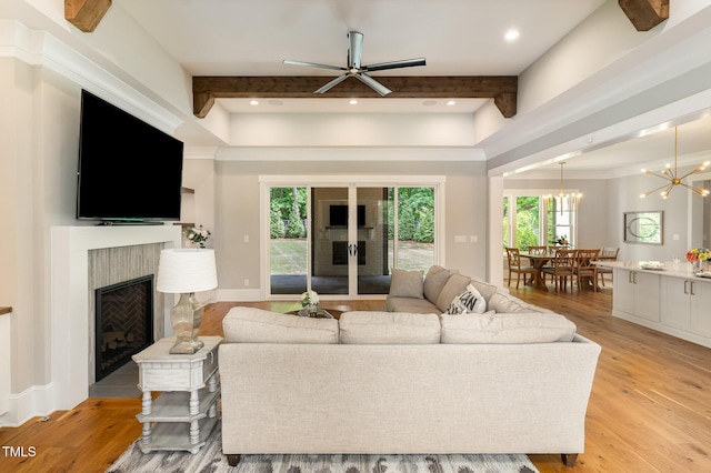 living room with a fireplace, light wood finished floors, beam ceiling, a chandelier, and a ceiling fan