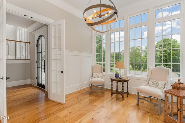 living area featuring light wood finished floors, a chandelier, wainscoting, and a decorative wall