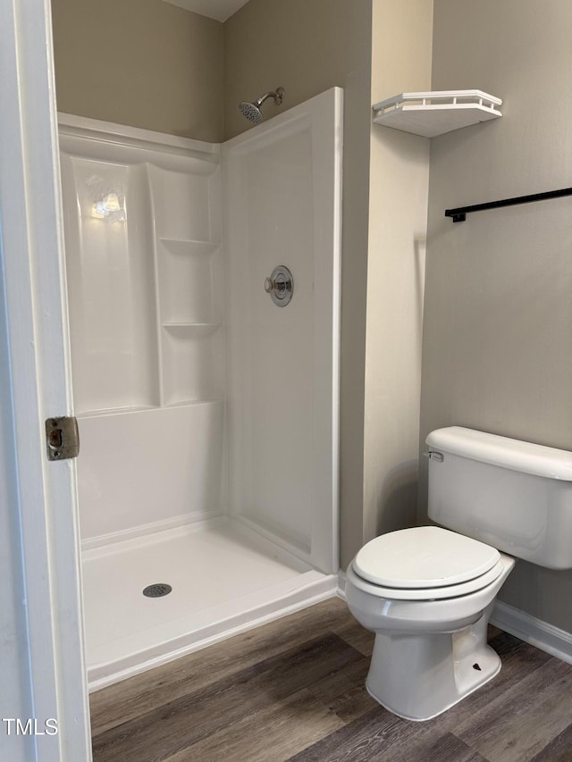 bathroom featuring a shower stall, wood finished floors, toilet, and baseboards