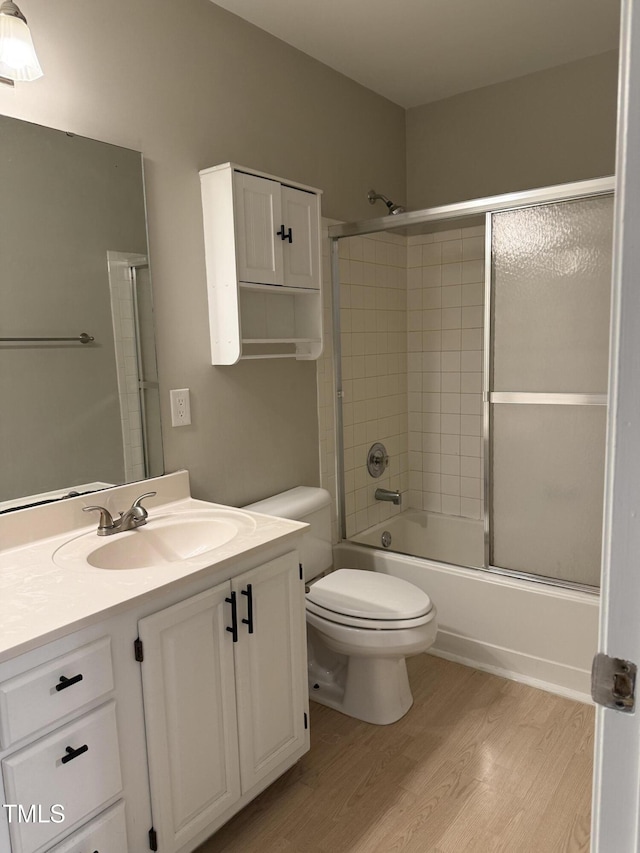 bathroom featuring wood finished floors, vanity, toilet, and bath / shower combo with glass door